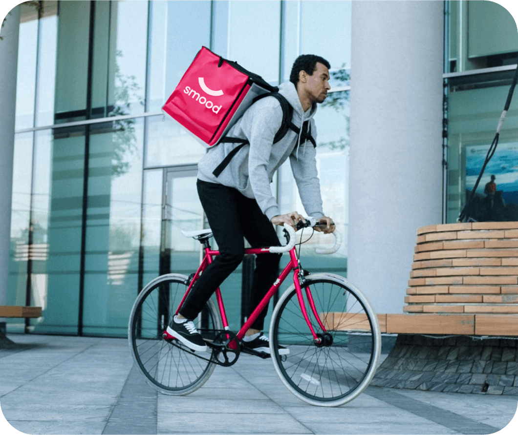 Livreur de repas Smood sur un vélo dans une rue de la ville, portant un sac à dos isotherme.