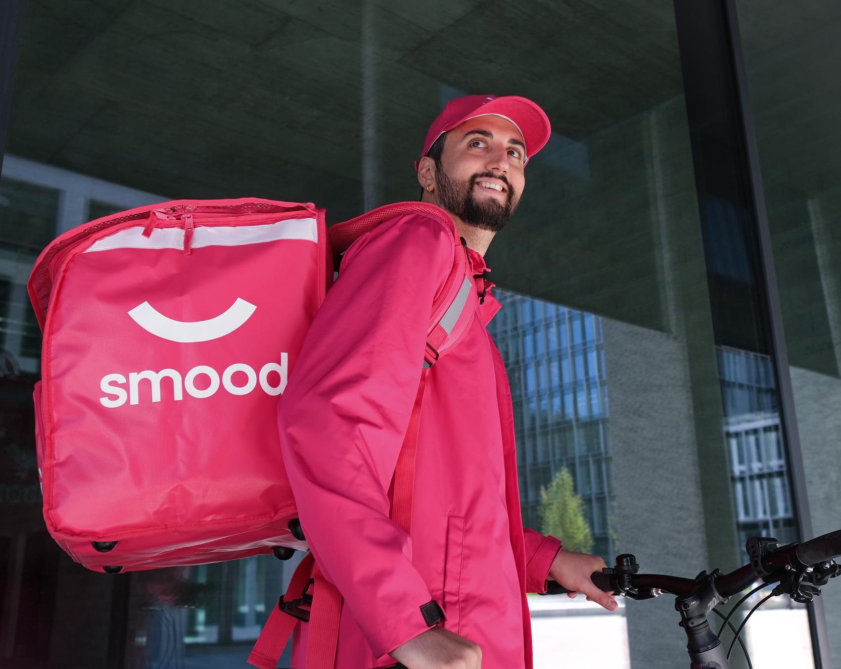 Livreur souriant portant un sac Smood, prêt à livrer des courses.